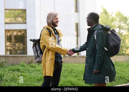 Two multiethnic colleagues greeting each other and smiling during meeting outdoors in the city Stock Photo