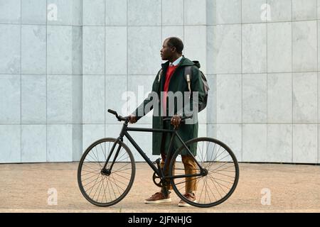 African mature businessman with backpack using his bike to get to the work standing outdoors and looking away Stock Photo