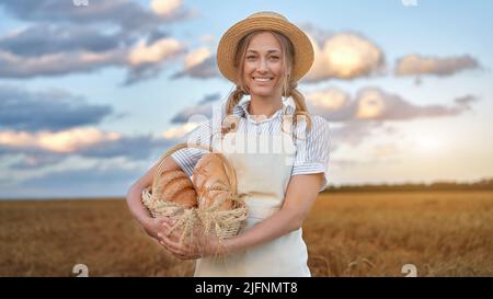 Woman baker holding wicker basket bread eco product Female farmer standing wheat agricultural field  Baking small business Caucasian person dressed st Stock Photo