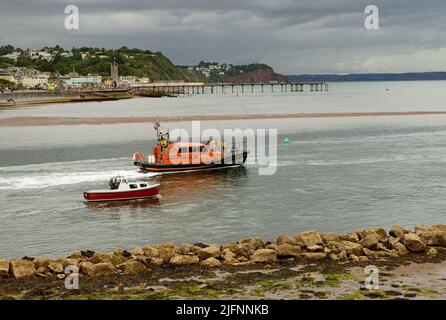 Beneath a threatening sky the RNLI Exmouth lifeboat leaves the Teign estuary between Teignmouth & Shaldon, and heads out to sea with another boat.. Stock Photo