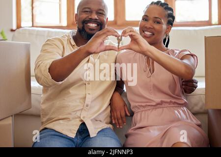 A couple holding keys, making a heart sign with their hands at home. Portrait of a smiling, happy african american man and woman in love, sitting in Stock Photo