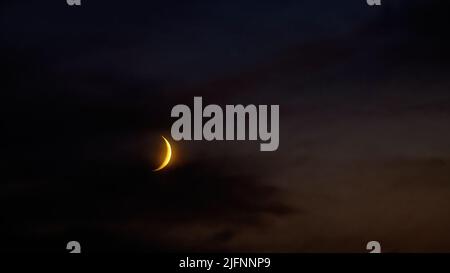 Growing moon in dark cloudy evening sky. Dark colors of summer night. Stock Photo