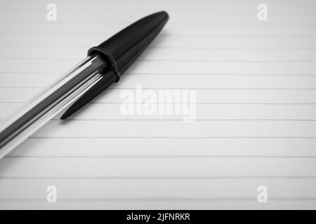 Close-up of a black pen resting on a lined paper sheet. Macro shot with selective focus and empty space for text Stock Photo