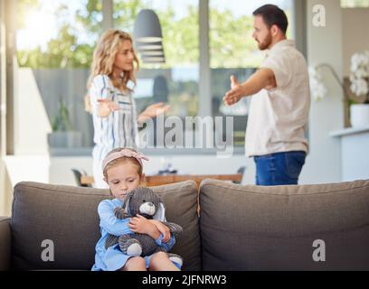 Kid feeling upset while parents argue in room. Couple arguing around child. Impact of family conflicts or divorce. Sad girl hugging teddybear Stock Photo