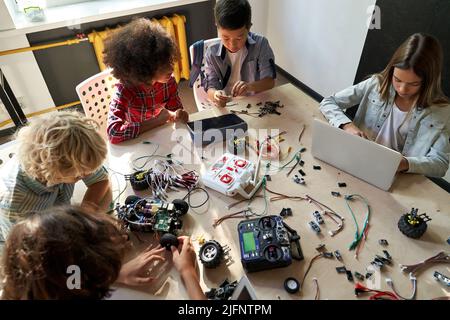Group of multiracial schoolkids at stem class building robot. Table top view. Stock Photo