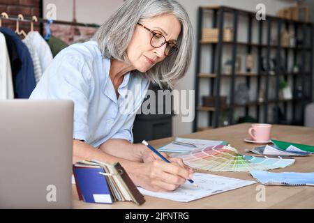 Senior middle aged fashion designer working in clothing design studio. Stock Photo