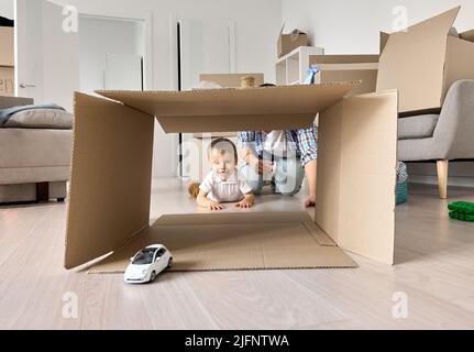 Happy kid son playing toy car with dad unpacking boxes on moving day. Stock Photo