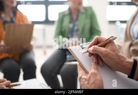 Elderly people attending group therapy session at nursing house, sitting in circle, having conversation with psychologist, close-up Stock Photo