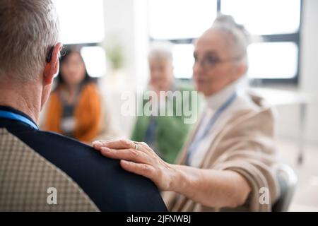 Group of senior people sitting in circle during therapy session, woman consoling depressed man. Stock Photo