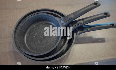 https://l450v.alamy.com/450v/2jfnwdh/concept-of-kitchen-utensils-close-up-of-new-set-of-frying-pans-lying-on-the-table-action-new-modern-non-stick-pans-2jfnwdh.jpg