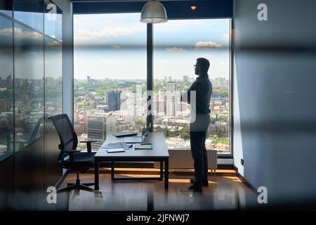Silhouette of businessman standing in office with big city capital urban view. Stock Photo