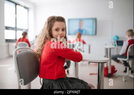 Happy schoolgirl wearing school uniform sitting in class and smiling in the camera. Stock Photo