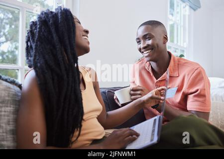 Happy young african american couple talking and bonding while sitting at home. Handsome man drinking coffee while girlfriend shops online. Smiling Stock Photo
