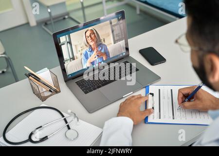 Indian male doctor in clinic consulting female patient using laptop computer. Stock Photo