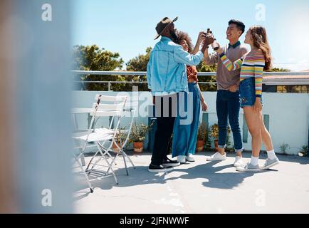 Full length of diverse group of young millennial friends standing outside together and toasting with beers. Smiling men and women being social and Stock Photo