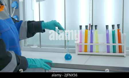 Woman conducts laboratory experiments and analyzes. Clip. Woman looks at chemical liquid in laboratory. Industrial laboratory with workers and Stock Photo