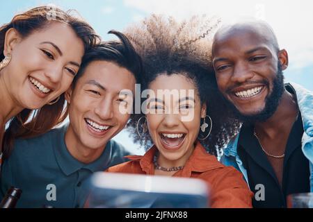 Diverse group of friends using cellphone to take selfies while bonding outside. African American woman with an afro smiling and taking pictures with Stock Photo