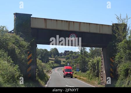 A red van approaches under a metal railway bridge. There is a height restriction of 4.2 meters on the bridge Stock Photo