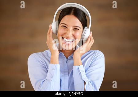 Happy young mixed race businesswoman wearing wireless headphones at work. One female only enjoying listening to relaxing music and songs, audio books Stock Photo