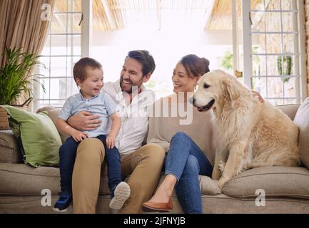 In my family, crazy is relative. All of them. Shot of a young family sitting on the living room sofa with their dog. Stock Photo