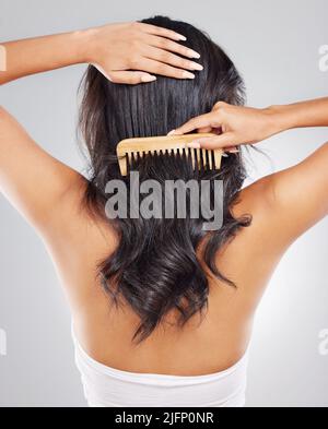 No knots allowed. Rearview shot of an unrecognizable young woman combing her hair against a grey background. Stock Photo
