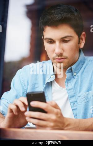 One mixed race handsome young man using his mobile phone while sitting outside in the city. Hispanic male texting and browsing social media while Stock Photo