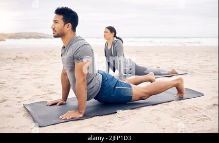 Opening up the chest while stretching the back. Shot of a sporty young couple doing an upward facing dog pose while practising yoga together on the Stock Photo
