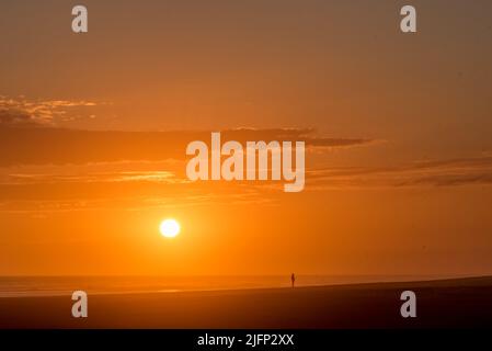 Man walking on the beach in golden sunset with the sun over the sea Stock Photo