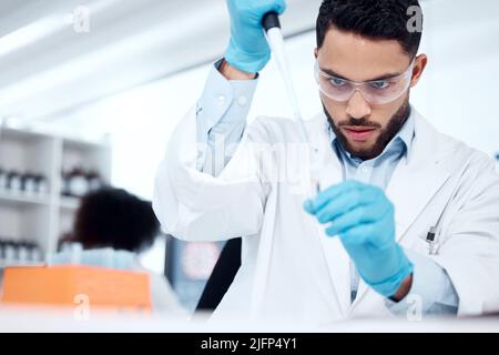 One mixed race male scientist wearing safety goggles and a labcoat while conducting a medical research experiment with pipette and test tubes in a lab Stock Photo