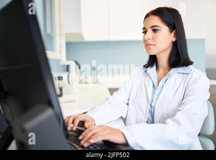 One confident and focused young caucasian doctor using a computer to browse the internet in a clinic. A medical professional wearing a labcoat and Stock Photo