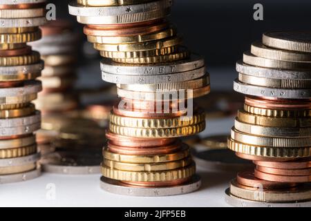 Piled up coins, Euros in different sizes leaning to the right on white surface and dark background Stock Photo