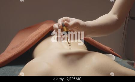 Close-up of oil dripping on back. Action. Masseur drips oil on back before massage. Massage with aromatic oils for relaxation Stock Photo