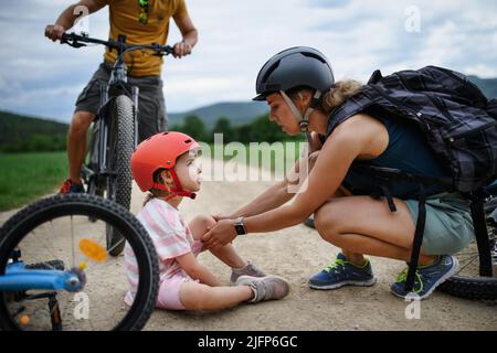 Mother and father helping their little daughter after falling off bicycle outdoors Stock Photo