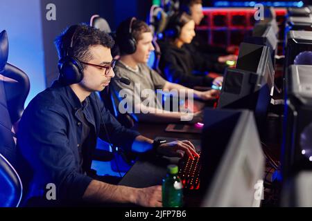 Side view at diverse cyber sport team playing video games in row, focus on Middle Eastern young man in foreground Stock Photo