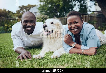 We enjoy our daily routine. Shot of a young couple lying on the grass with their dog in their garden at home. Stock Photo