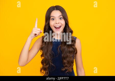 Excited face, cheerful emotions of teenager girl. Portrait of young teenager pointing up with finger, isolated on yellow background. Funny school girl Stock Photo