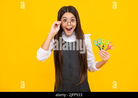 Excited amazed teenage girl with scissors, isolated on yellow background. Child creativity, arts and crafts. Stock Photo