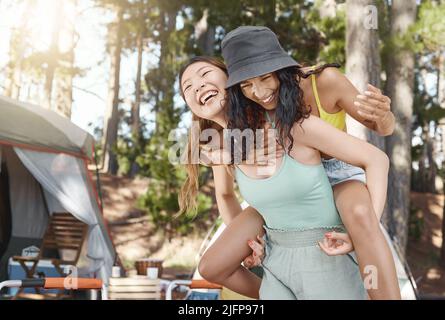 Staying young at heart. Shot of an attractive young woman giving her friend a piggyback ride during a day in the woods. Stock Photo
