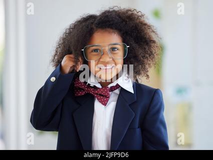 Go on, Im listening. Shot of an adorable little girl dressed as a businessperson standing alone in an office. Stock Photo