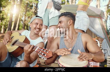 You know what song Im thinking of. Shot of two handsome men sitting and playing musical instruments during a day in the woods with friends. Stock Photo