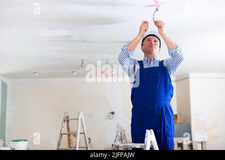 Man electrician standing on stepladder and fixing wires Stock Photo