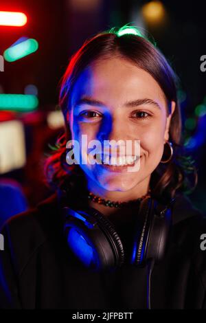 Vertical closeup portrait of young woman on cyber sports team smiling at camera cheerfully lit by neon light Stock Photo