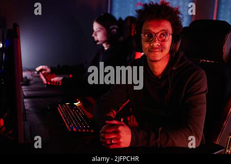 Portrait of black young gamer looking at camera in red neon light and smiling, copy space Stock Photo