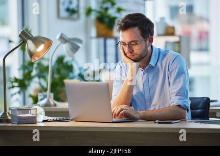 When did it become so boring. Shot of a young businessman looking bored while sitting at his desk. Stock Photo