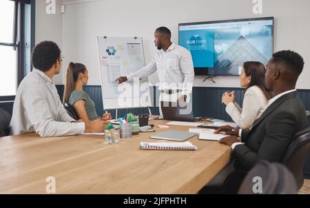 A group of young diverse corporate business people working as a team on a project in a boardroom. African American man speaker using a chart and graph Stock Photo