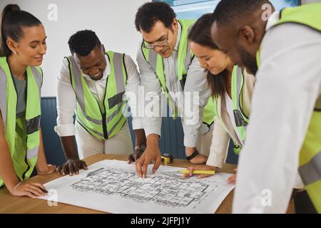 Closeup of a happy diverse multiracial group of architect colleagues analyzing a blueprint design on a building and discussing plans for the next Stock Photo
