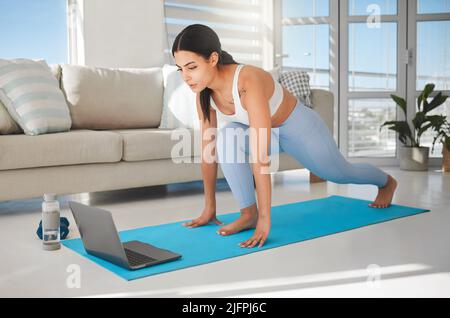 Starting another session online with her personal trainer. Shot of a sporty young woman using a laptop and doing lunges while exercising at home. Stock Photo