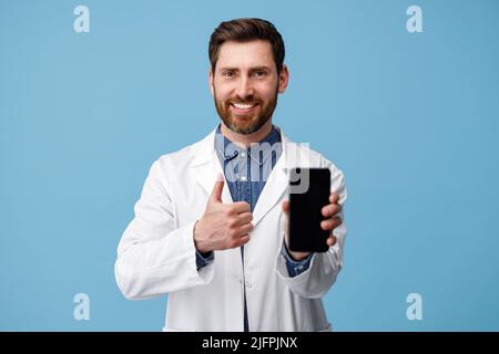 General Practitioner showing thumb up to empty cellphone screen standing over blue background Stock Photo