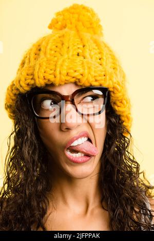 Yellow is such a playful colour. Shot of an attractive young woman standing alone in the studio and pulling funny faces while wearing a beanie. Stock Photo