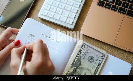 Woman counting money and making notes in notepad Stock Photo